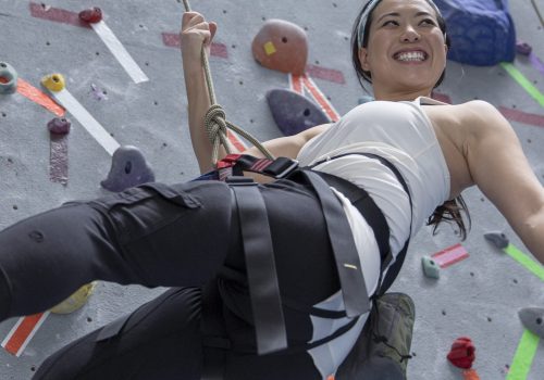 Happy woman hanging from rope at rock wall in climbing gym